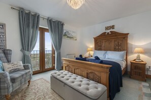 A bedroom with a bed, a wooden dresser, a bench, a chair, and a balcony with curtains.