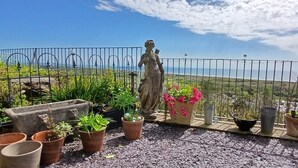 A balcony with a statue, potted plants, and a view of the sea.