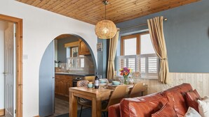 A cozy interior with a dining area, a leather sofa, and a kitchen visible through an archway.