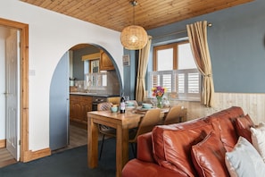 A cozy interior with a dining area, a leather sofa, and a kitchen visible through an archway.