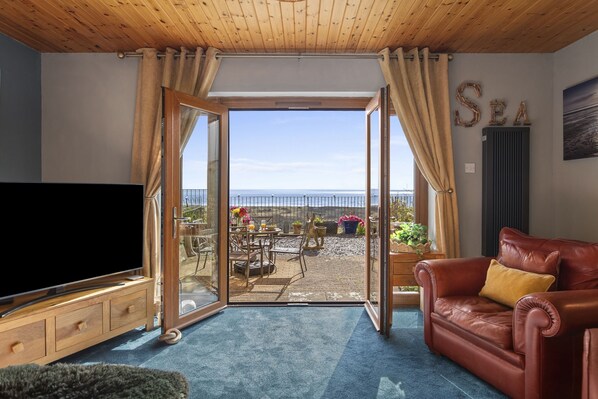 Una habitación con televisión, un sofá de cuero, una zona de comedor con asientos exteriores y vista al mar.
