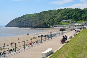 A coastal beach with a promenade, benches, and a grassy area.