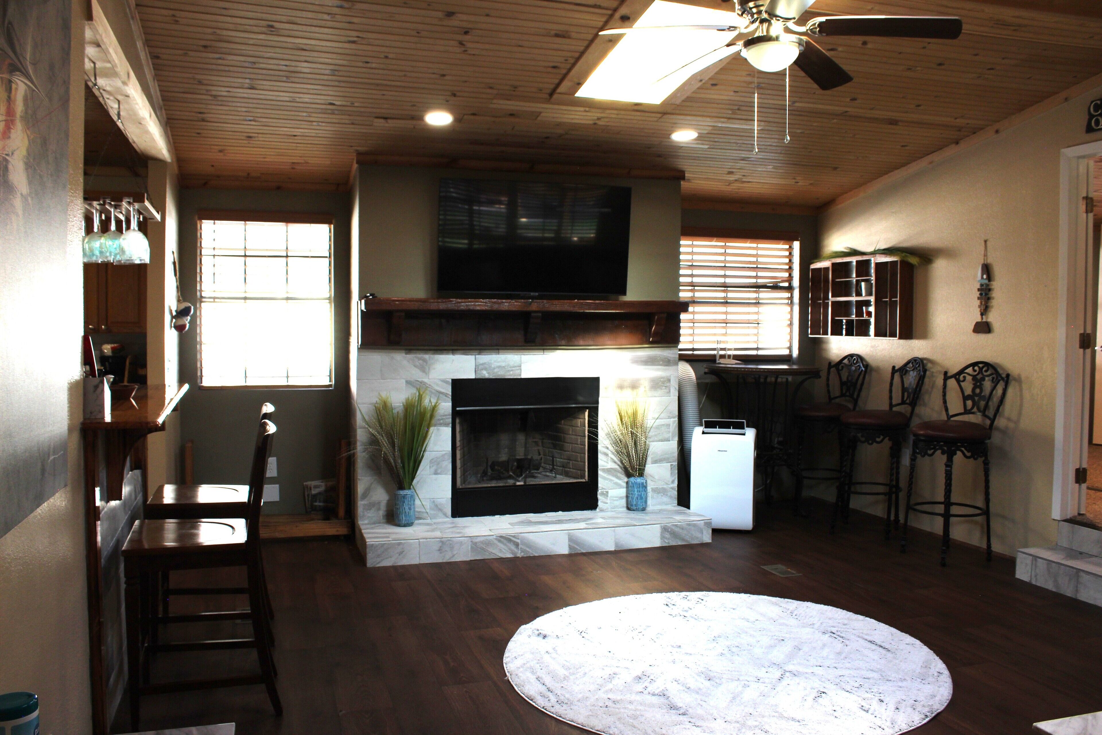 A living room with a fireplace, wooden ceiling, and a round rug.