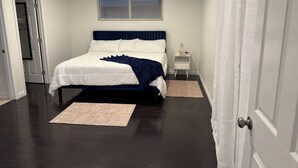 A bedroom with a bed, bedside tables, a window with blinds, and a door. - Riverside Dream House (Riverside)