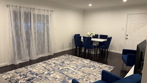 A dining area with a table, four chairs, a rug, and a door. - Riverside Dream House (Riverside)