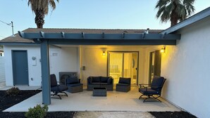 A covered patio area with outdoor seating and a sliding glass door leading to an interior space. - Riverside Dream House (Riverside)