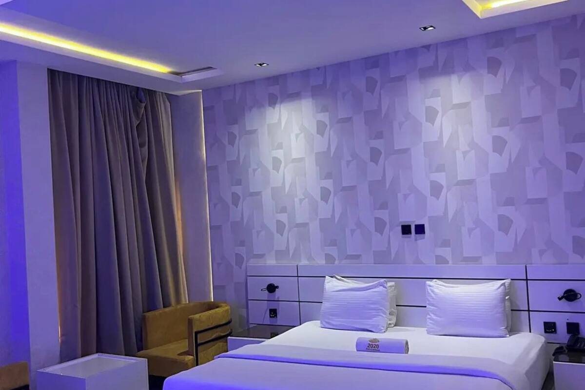 A modern hotel room with a large bed, a nightstand, a chair, and a wall with a geometric pattern.