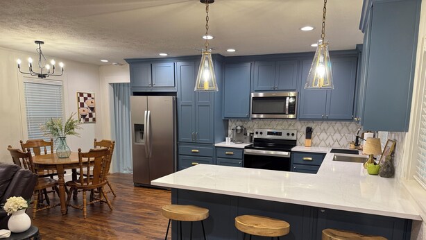 A modern kitchen with dark blue cabinets, a stainless steel refrigerator, a microwave, and a large island with bar stools. - 3 bedroom house just 1 mile from the heart of historic downtown Waxahachie! (Waxahachie)