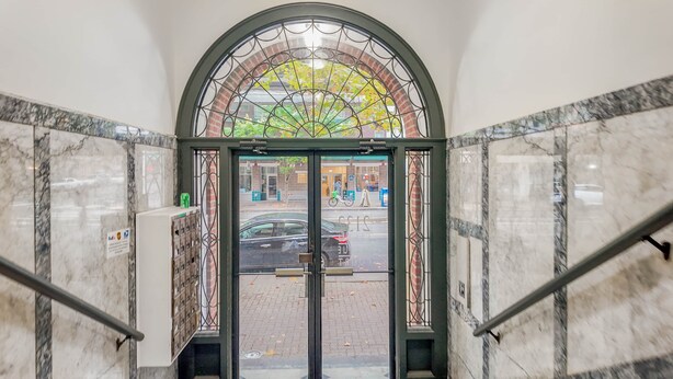 Un escalier en marbre mène à une porte dotée d’un panneau de verre et de barreaux en métal, et donne sur la rue.