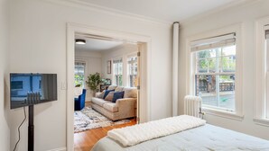 Une chambre à coucher avec un lit, une télévision, une fenêtre donnant sur la rue et une porte menant à une autre pièce.
