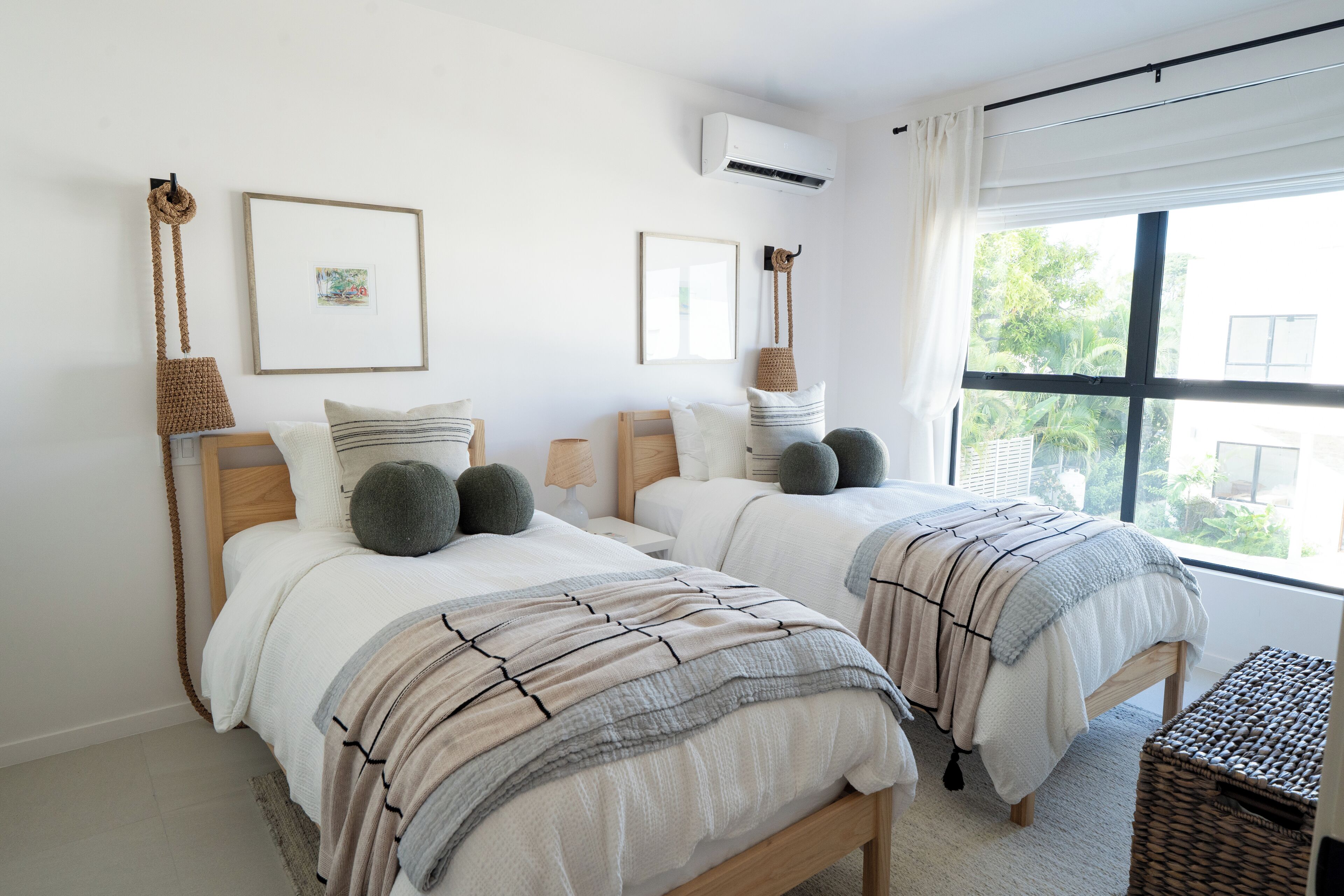 A bedroom with two beds, a large window, and a woven basket.