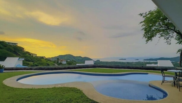 A swimming pool with a curved design surrounded by grass and a view of the ocean. - Endless Ocean Views 4 bedroom suites, Private Pool, minutes from downtown Coco (Coco)