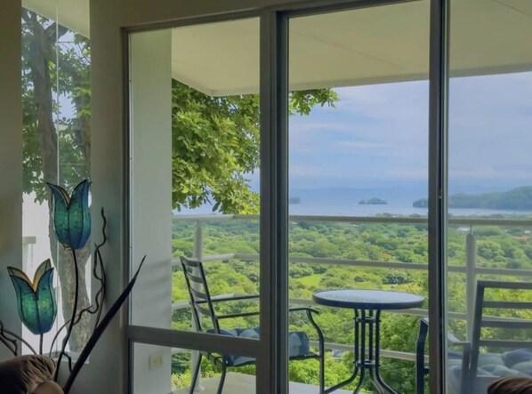 A balcony with a table and chairs, overlooking a lush landscape with trees and a distant view of the sea. - Endless Ocean Views 4 bedroom suites, Private Pool, minutes from downtown Coco (Coco)