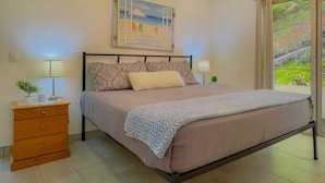 A bedroom with a bed, a nightstand, a dresser, a ceiling fan, and a window with a view of greenery. - Endless Ocean Views 4 bedroom suites, Private Pool, minutes from downtown Coco (Coco)
