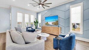 Un salon moderne doté d’un ventilateur de plafond, d’un grand téléviseur et offrant une vue sur l’extérieur grâce à une fenêtre.