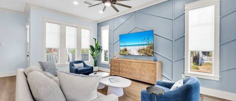 Una sala de estar moderna con un ventilador de techo, un televisor grande y vistas al exterior a través de una ventana.