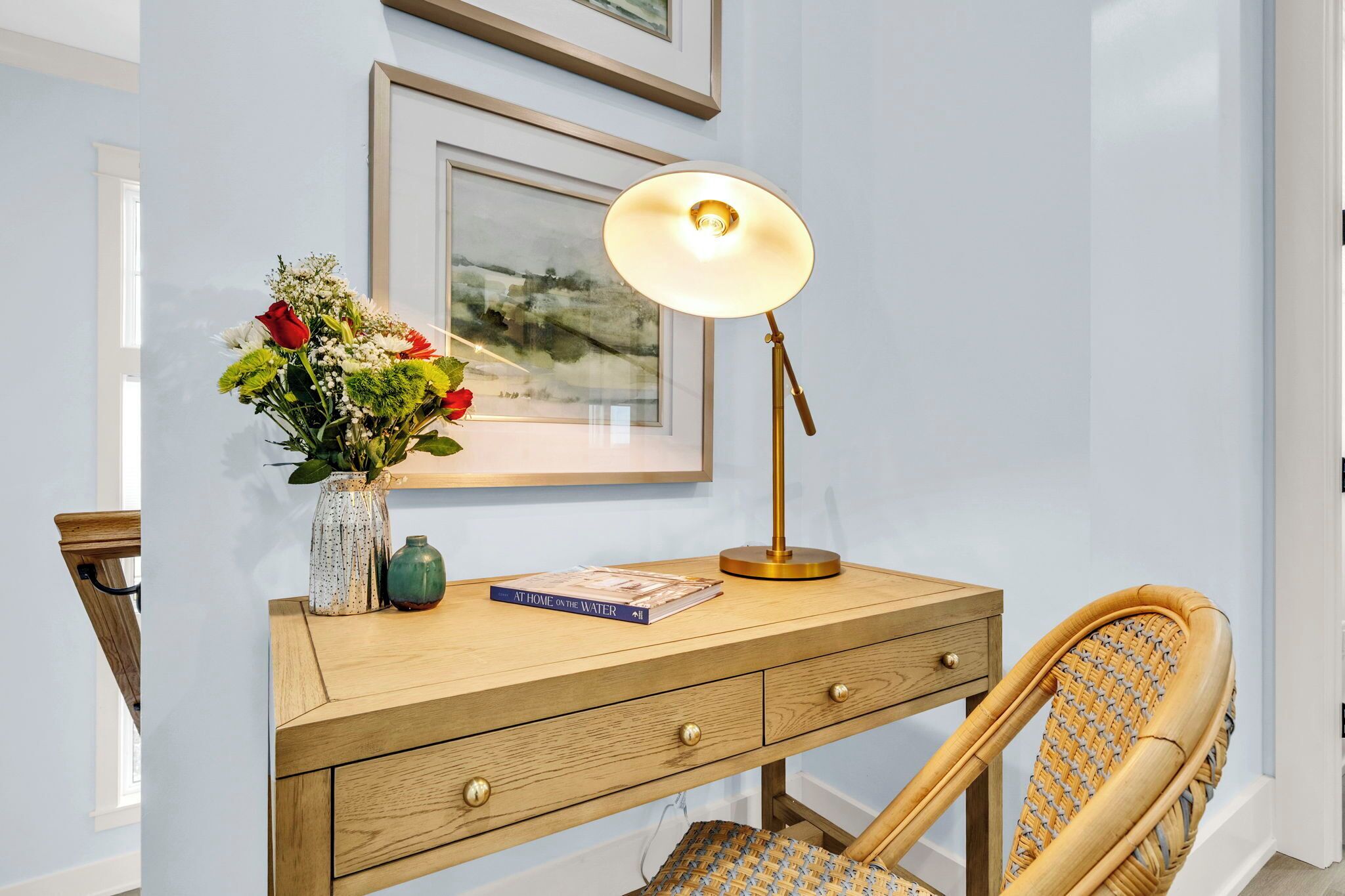 A wooden desk with a lamp, a vase with flowers, and a book titled "At Home in the Water".