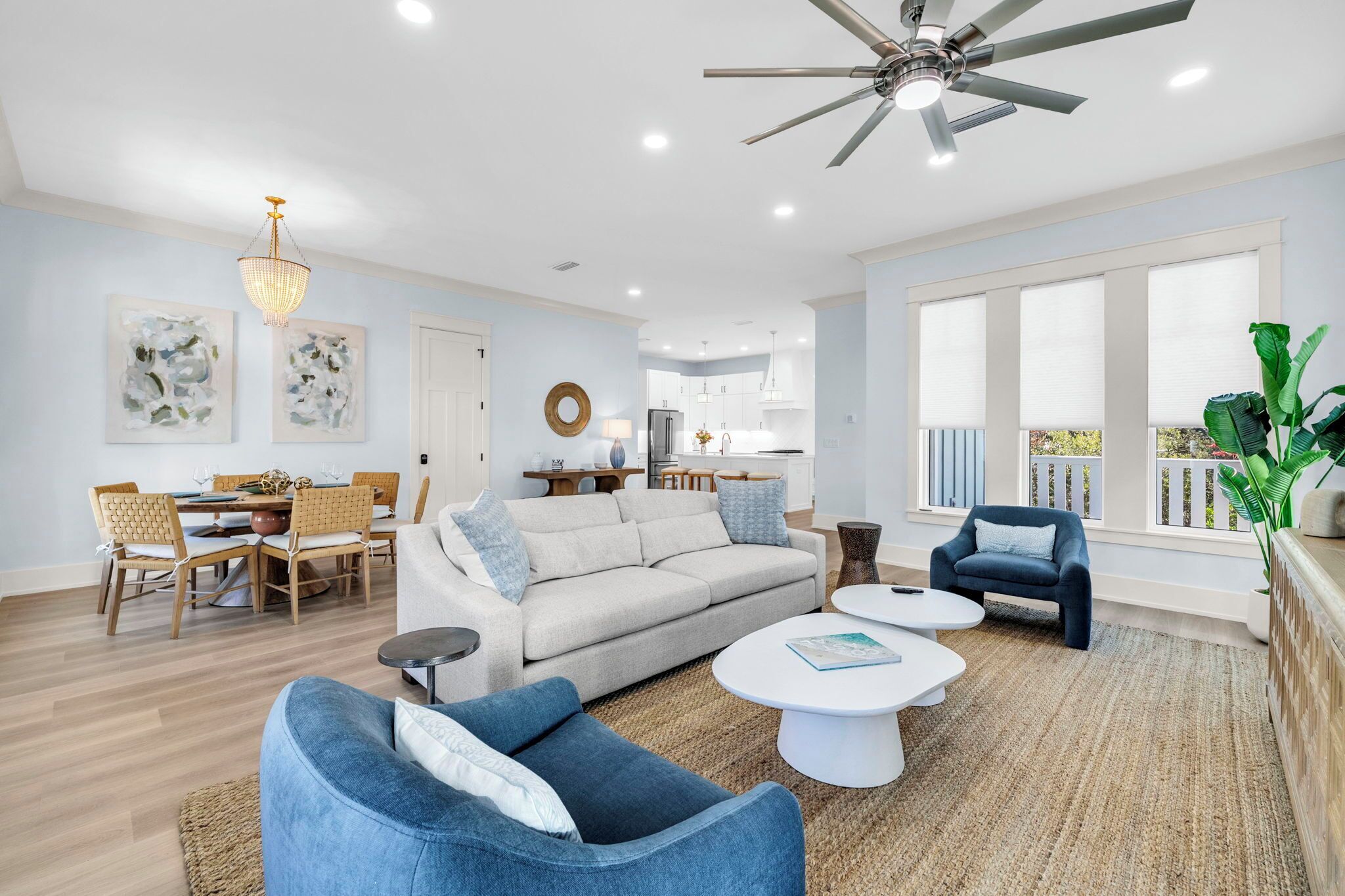 A spacious living room with a sofa, coffee table, and armchairs, a dining area with a table and chairs, and a kitchen in the background.