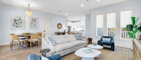 A spacious living room with a sofa, coffee table, and armchairs, a dining area with a table and chairs, and a kitchen in the background.