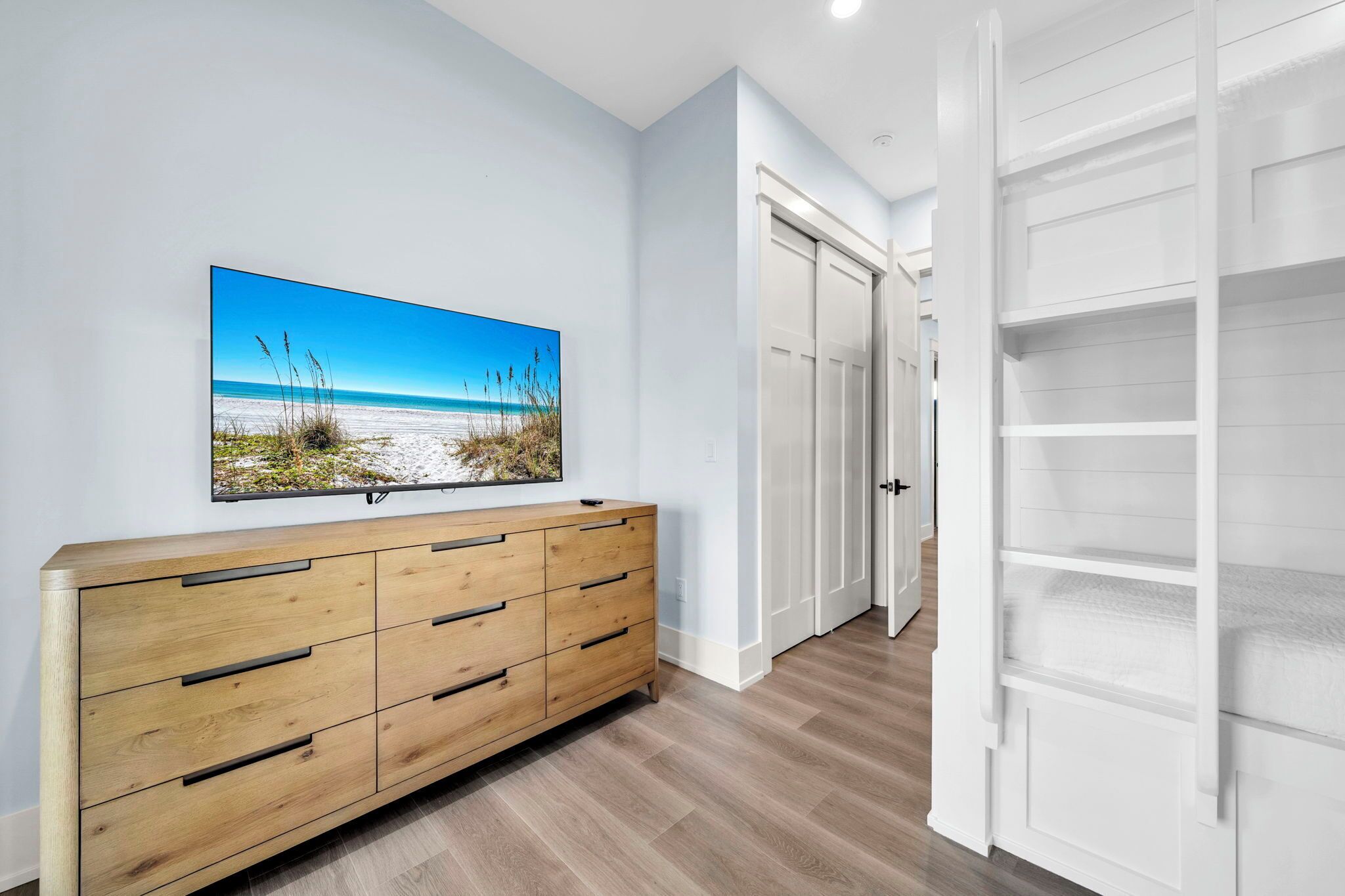 A hallway with a wooden dresser, a large framed picture of a beach, and white doors.