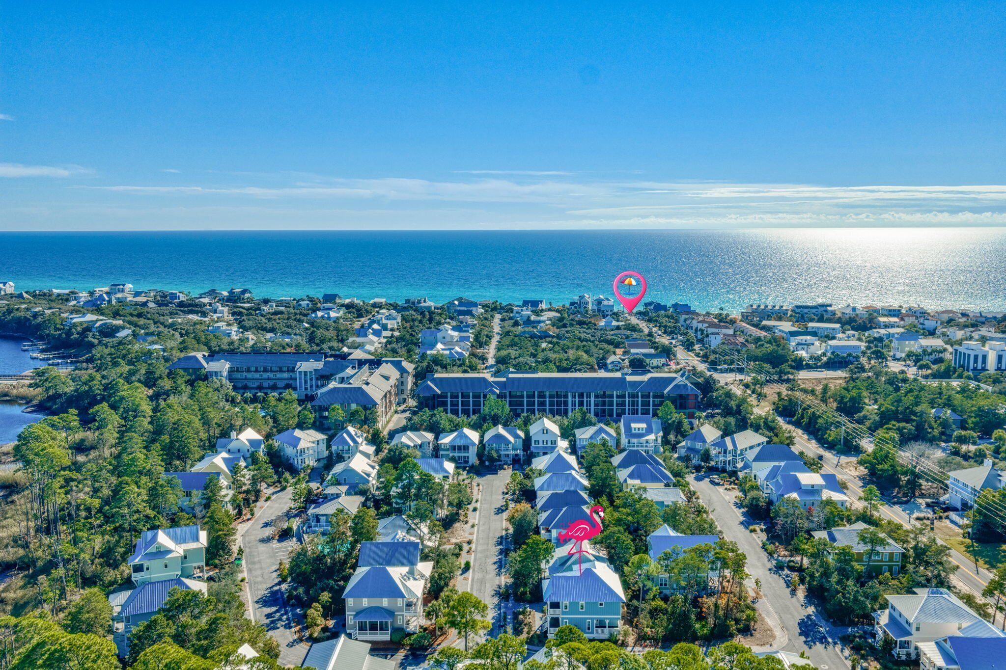 An aerial view of a coastal residential area with houses, a large building, and a flamingo statue.