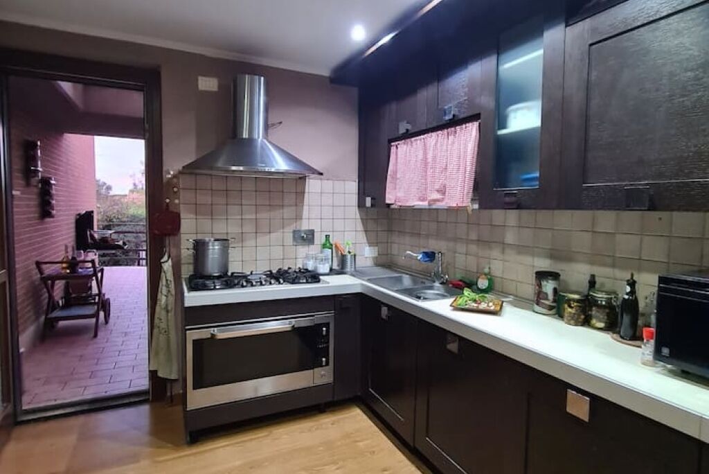 Una cucina con mobili scuri, una cappa aspirante in acciaio inossidabile, un forno integrato e un piano di lavoro bianco con diversi oggetti da cucina.