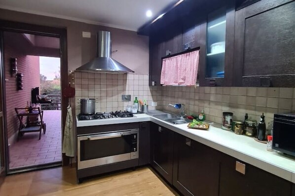 A kitchen with dark cabinets, a stainless steel range hood, a built-in oven, and a white countertop with various kitchen items.