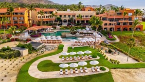 A resort with a large pool, multiple lounge areas with umbrellas, and a mountainous backdrop. - Oceanview Penthouse Casa Del Mar (San José del Cabo)