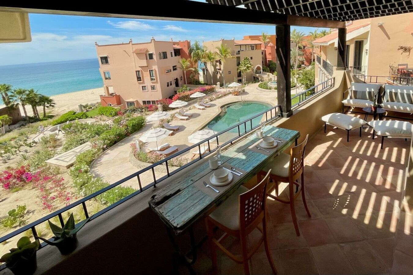 A balcony with a view of a pool, lounge chairs, and a beach.