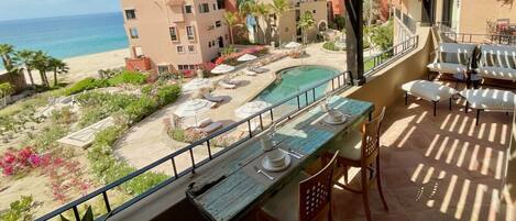 A balcony with a view of a pool, lounge chairs, and a beach.