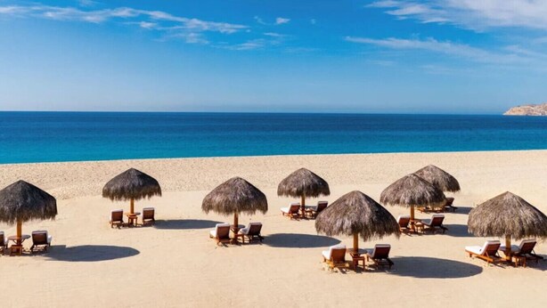 A beach with rows of sun loungers and thatched umbrellas, facing a calm sea under a clear sky. - Oceanview Penthouse Casa Del Mar (San José del Cabo)