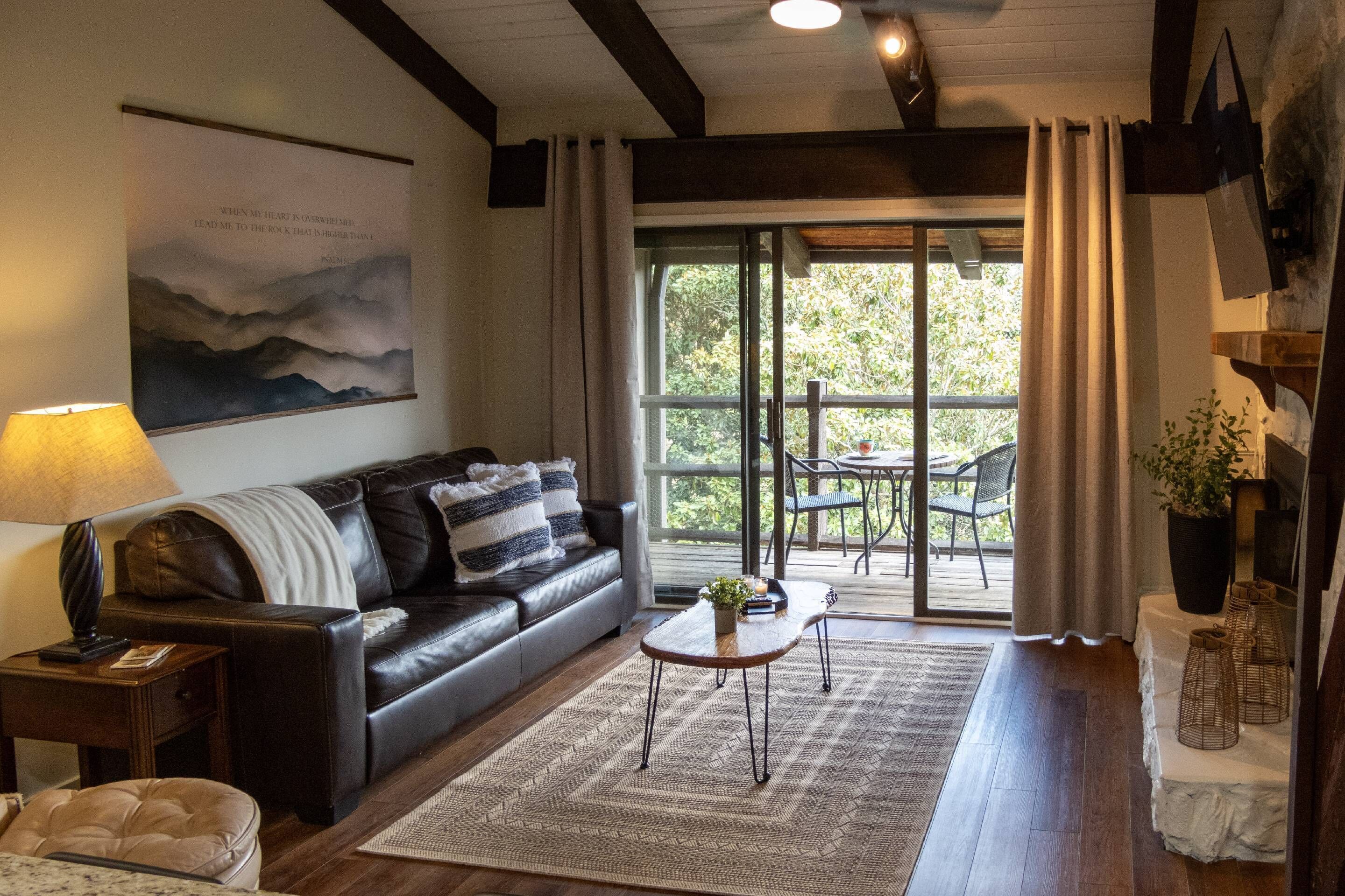 Ein Wohnzimmer mit einer Ledersofa, einem Couchtisch, einem Teppich und einem großen Fenster mit Vorhängen.