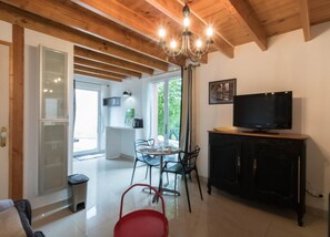 Une pièce avec un plafond en bois, un téléviseur posé sur un meuble, une table à manger avec des chaises et une fenêtre donnant sur un paysage verdoyant.