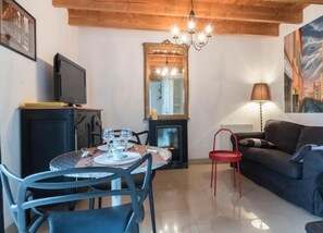 Uma sala de estar aconchegante com lareira, um espaço de jantar com mesa posta para dois e uma televisão em um móvel.