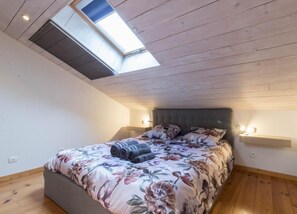 Une chambre avec un puits de lumière, un lit avec une literie à motifs floraux, un plancher en bois et deux lampes de chevet.