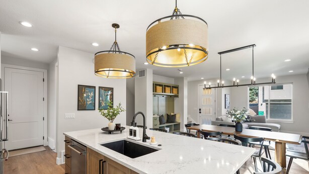 A modern kitchen with a large island, pendant lighting, and wooden cabinets.
