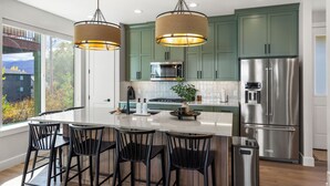 A modern kitchen with a central island, stainless steel appliances, and green cabinets.