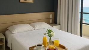 A hotel room with a bed, a bedside table, a tray with breakfast items, an air conditioner, and a window with curtains.