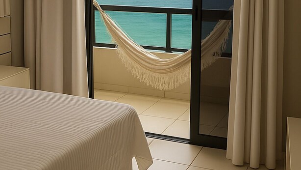 A hotel room with a bed, a view of the ocean through a glass door, and a hammock.