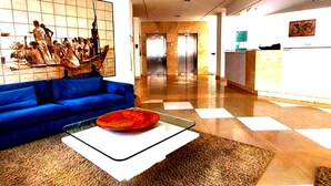 A modern lobby with a blue sofa, a glass coffee table, and a patterned rug.