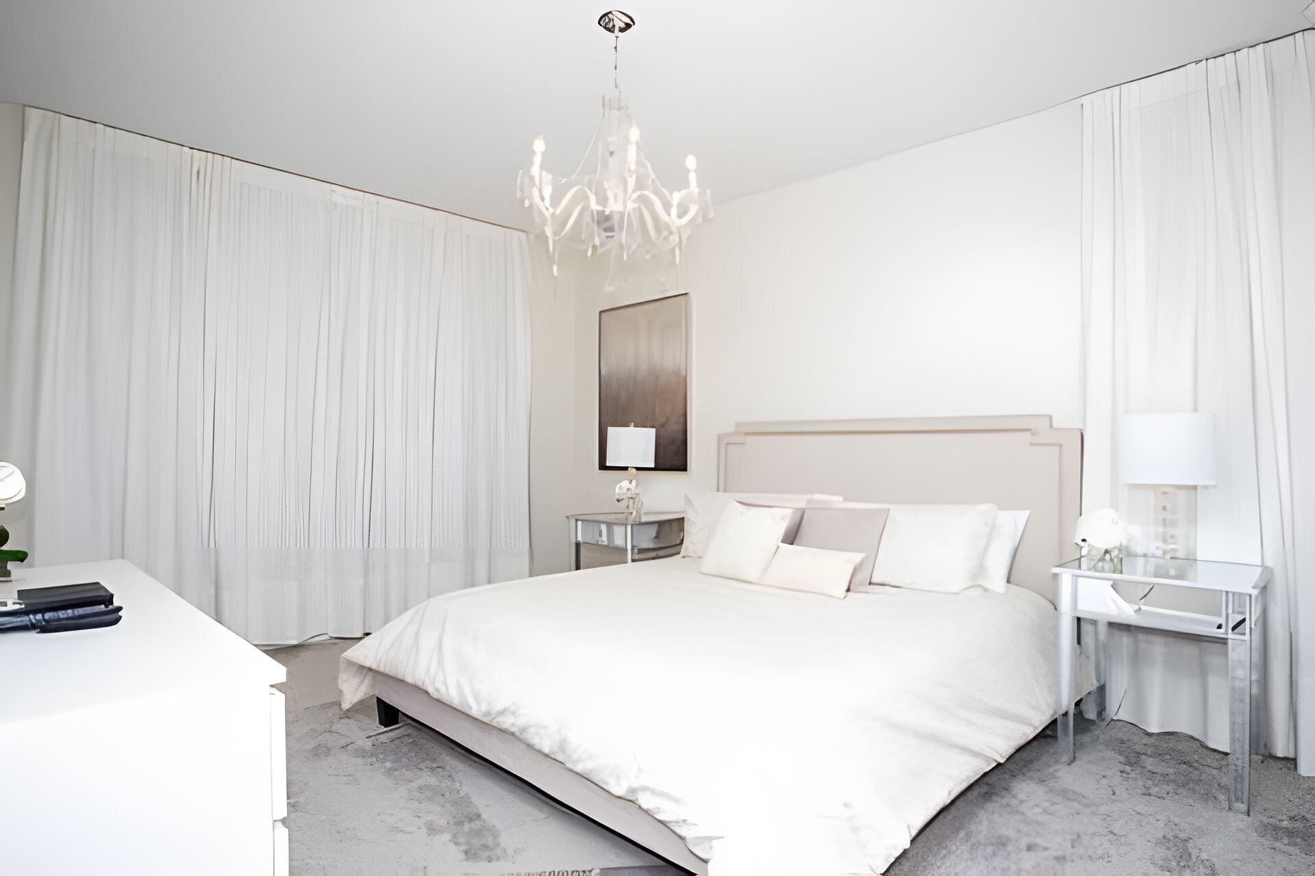 A modern hotel bedroom with a large bed, a chandelier, and a nightstand with a lamp.