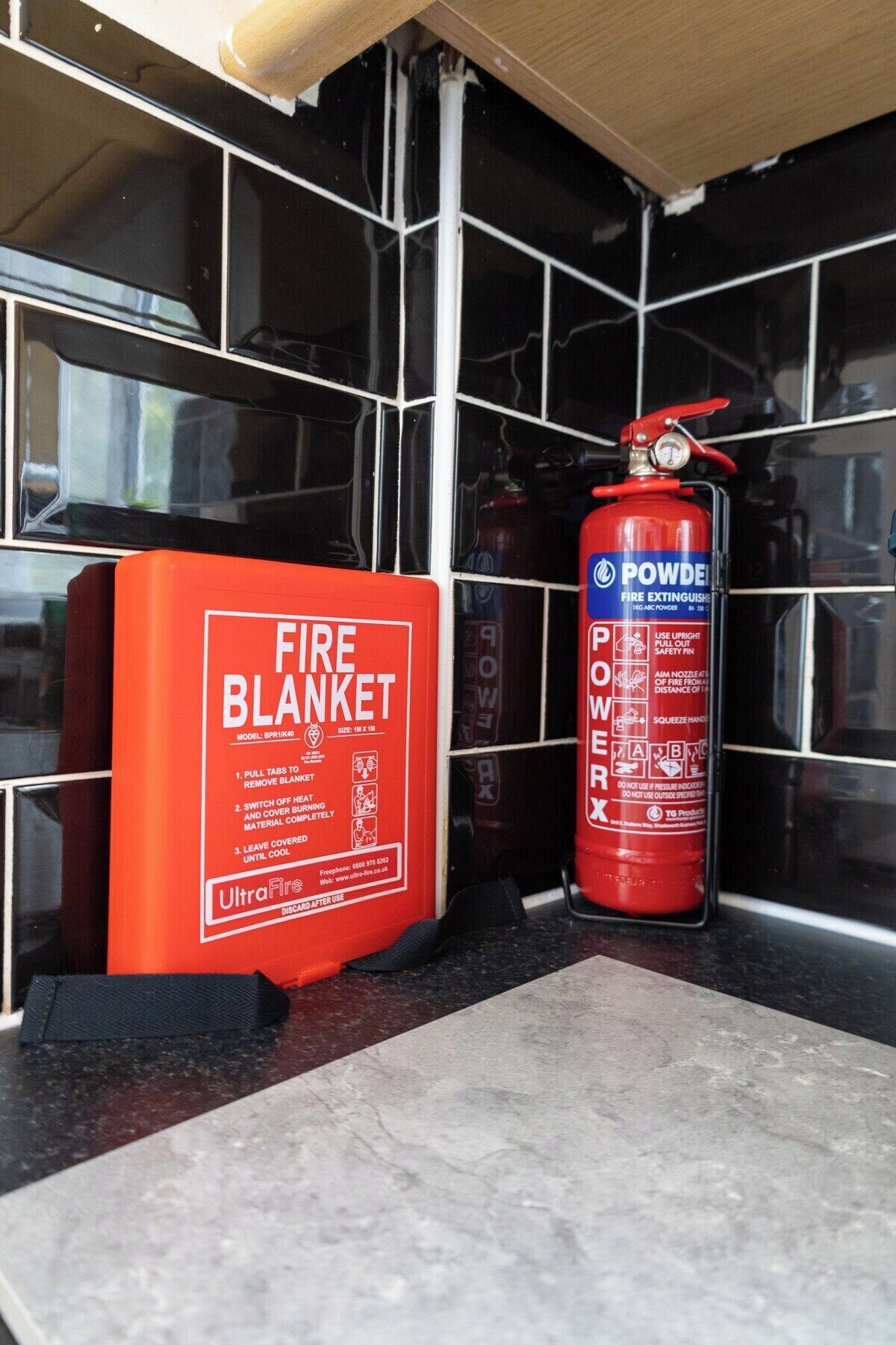 A fire blanket and a fire extinguisher on a tiled wall.