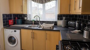 A kitchen with wooden cabinets, a washing machine, a sink, and a stove. - Modern 3-bed Bradley Stoke Self Check-in Free Parking Fast Wi-Fi (Bradley Stoke)