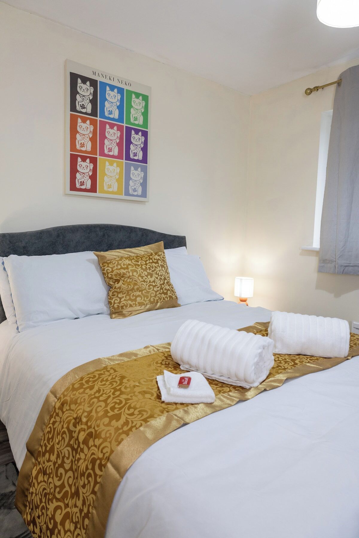 Ein Hotelzimmer mit einem großen Bett, zwei Kissen, einem Kopfteil, einem Nachttisch mit Lampe und einem Wandbild.