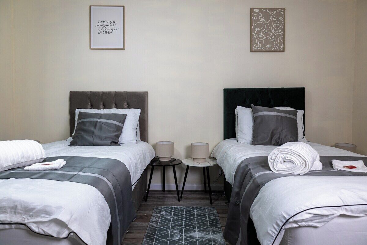 A hotel room with two beds, each with a headboard, a small table between them, and a rug on the floor.