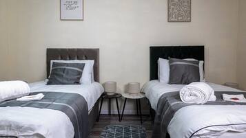 A hotel room with two beds, each with a headboard, a small table between them, and a rug on the floor.