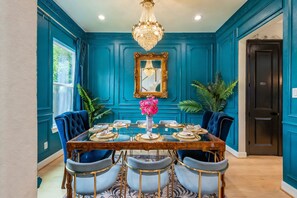 A dining room with a wooden table set for six, surrounded by blue upholstered chairs, a chandelier, and a mirror on the wall.