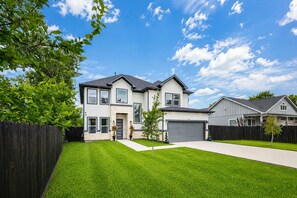 A two-story house with a garage, a well-maintained lawn, and a wooden fence.