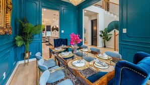 A dining area with a long table set for six, blue upholstered chairs, and a chandelier.