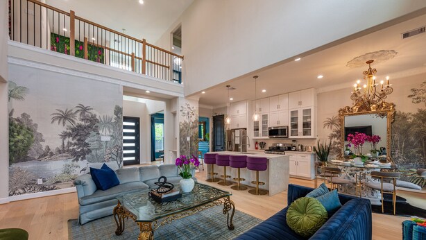 A spacious living area with a high ceiling, a dining area with bar stools, a kitchen with white cabinets, and a large mirror.